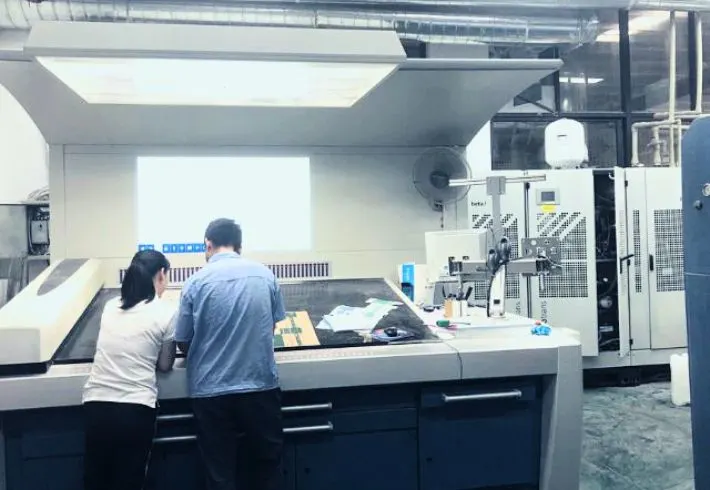 Quality Control Specialists Inspecting The Print Quality And Color Accuracy Of Mailer Box Samples In The Factory